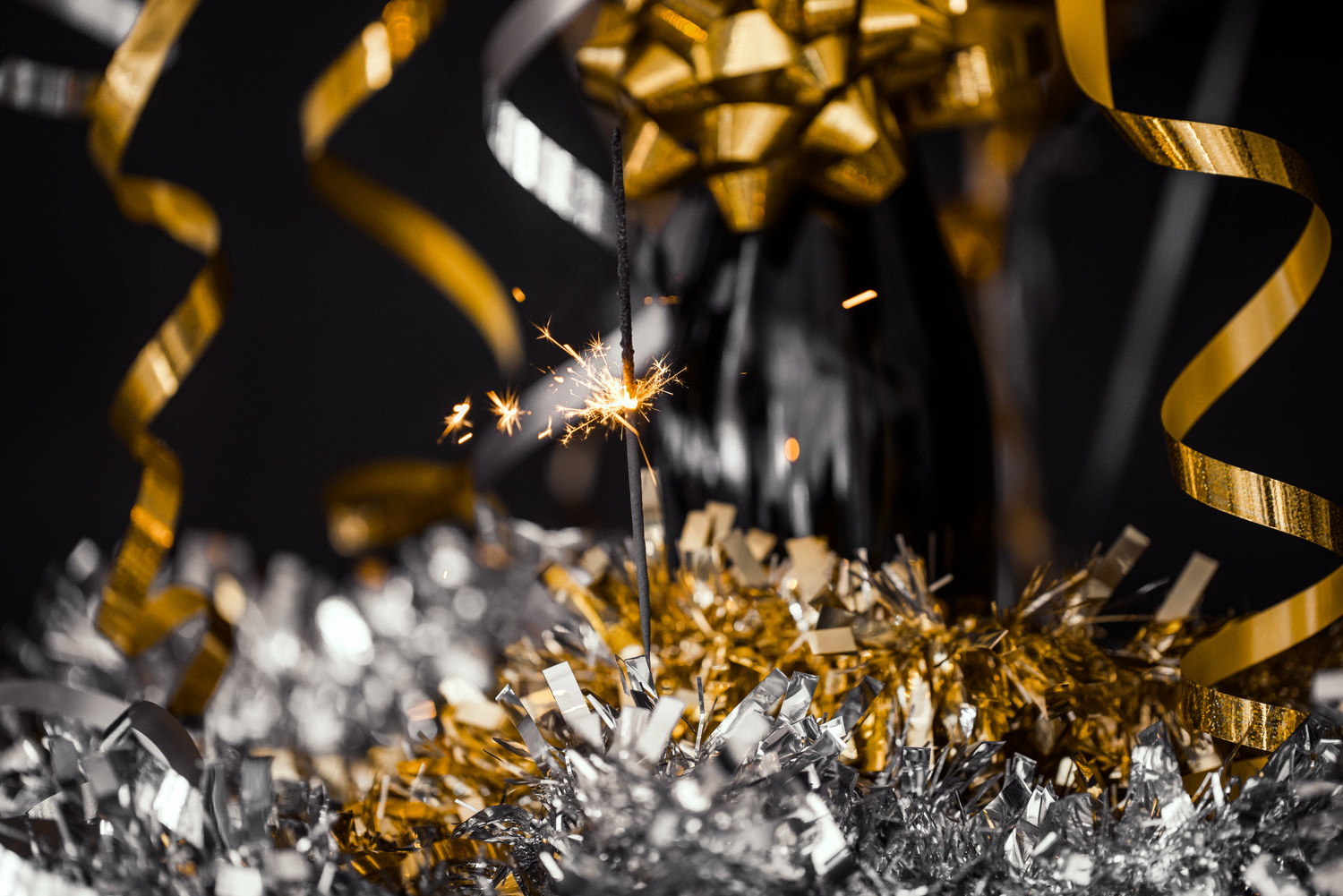 This image features a lit party sparkler emitting a bright glow, surrounded by shiny decorative elements like confetti or tinsel. The overall mood of the image is festive and celebratory